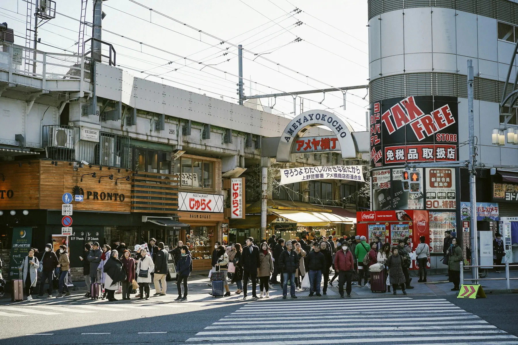 Calle principal del mercado Ameyoko en Ueno, Tokio, de día con tiendas abiertas, puestos de comida callejera, letreros de colores y gente comprando frutas secas y productos frescos
