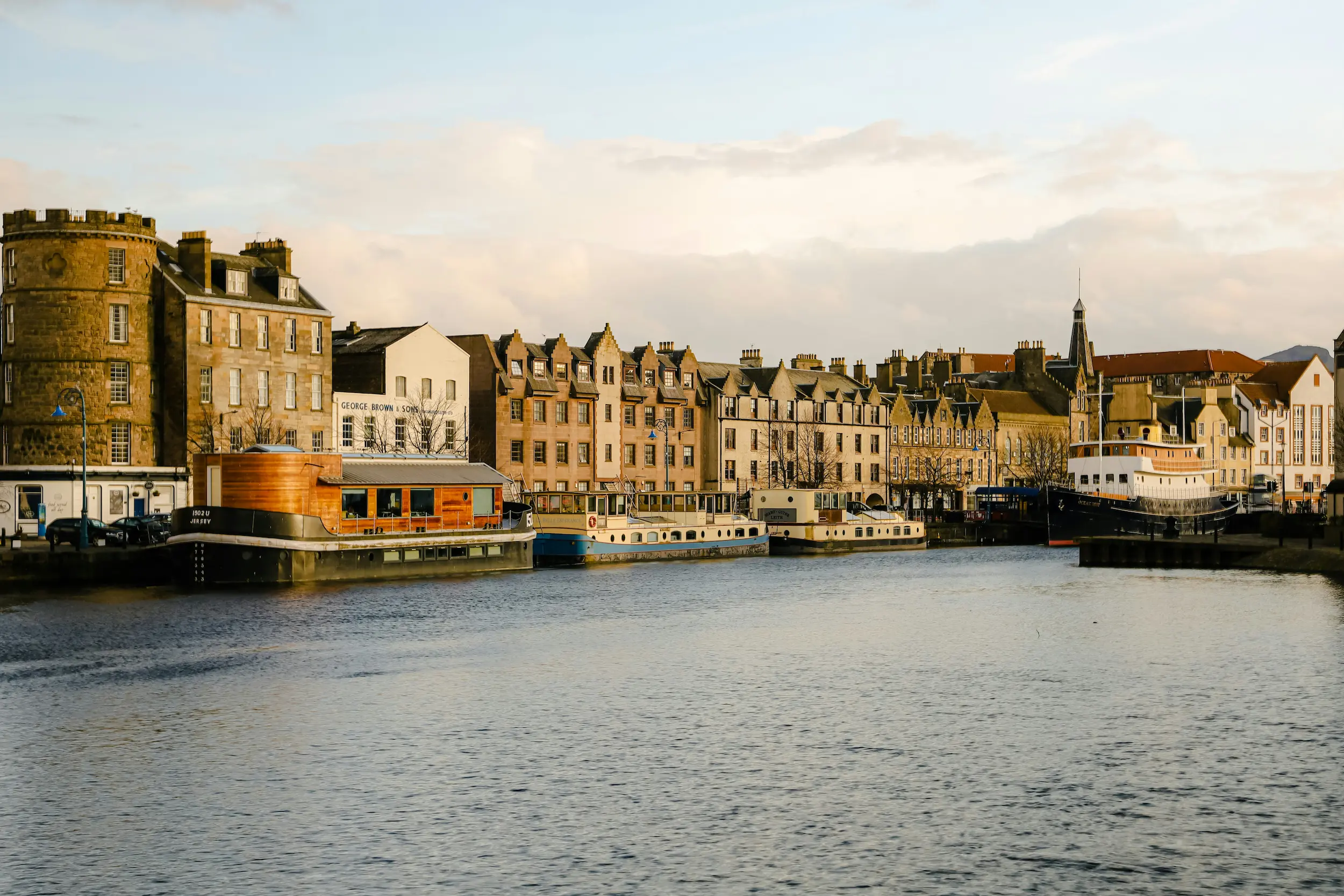 Vista del puerto de Leith en Edimburgo con casas históricas de colores junto al agua y barcos amarrados al atardecer