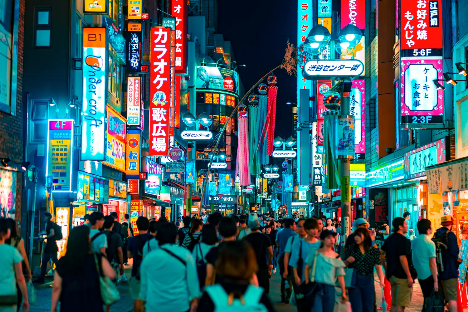 Calle abarrotada de gente caminando de noche en Tokio, Japón, con edificios iluminados por enormes anuncios de neón y pantallas digitales de colores brillantes