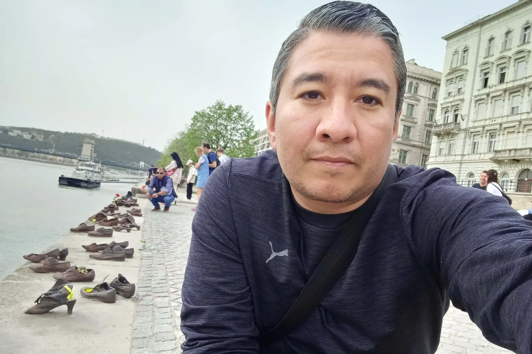 Persona de espaldas mirando los zapatos de hierro del memorial del Holocausto en la orilla del río Danubio en Budapest, con el agua y un puente al fondo.