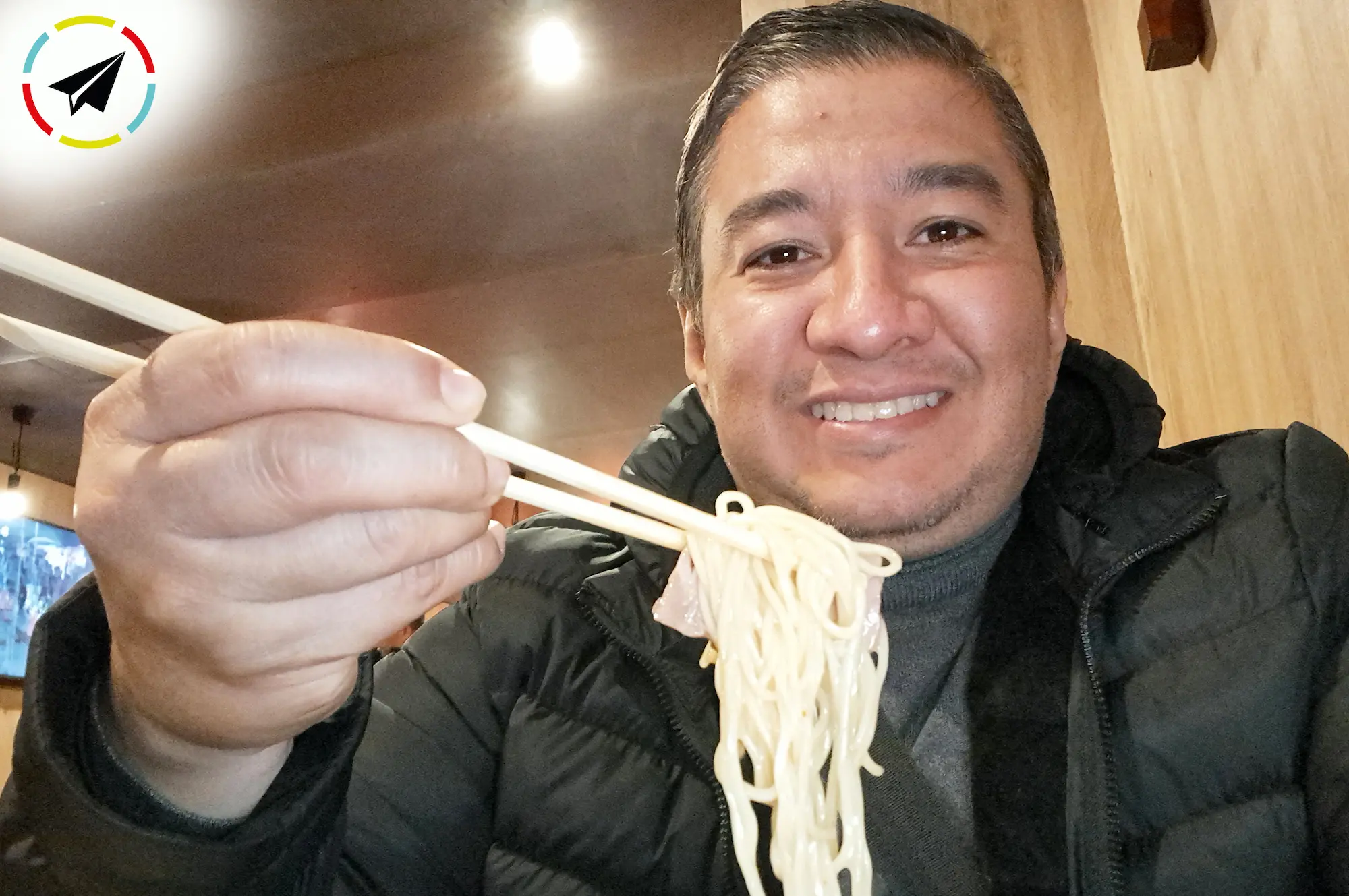 sosteniendo fideos de ramen con los palillos sobre un bol humeante de caldo tonkotsu en Ichiran, Japón, antes del primer sorbo.