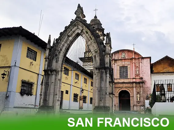 Vista completa de la Iglesia de San Francisco en Uruapan, Michoacán, mostrando la fachada de cantera, la torre campanario y el atrio con árboles.