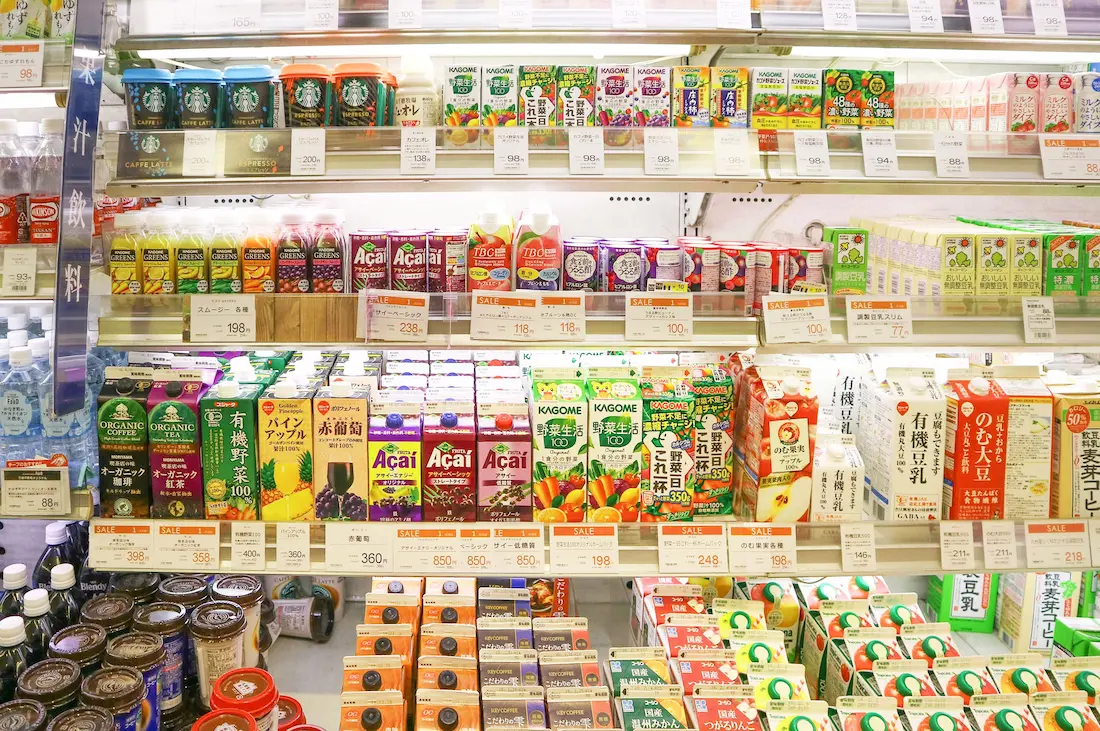 Estantería de un konbini japonés con una gran variedad de bebidas frías y calientes, llenando una pared entera con botellas de té, café, jugos y bebidas deportivas