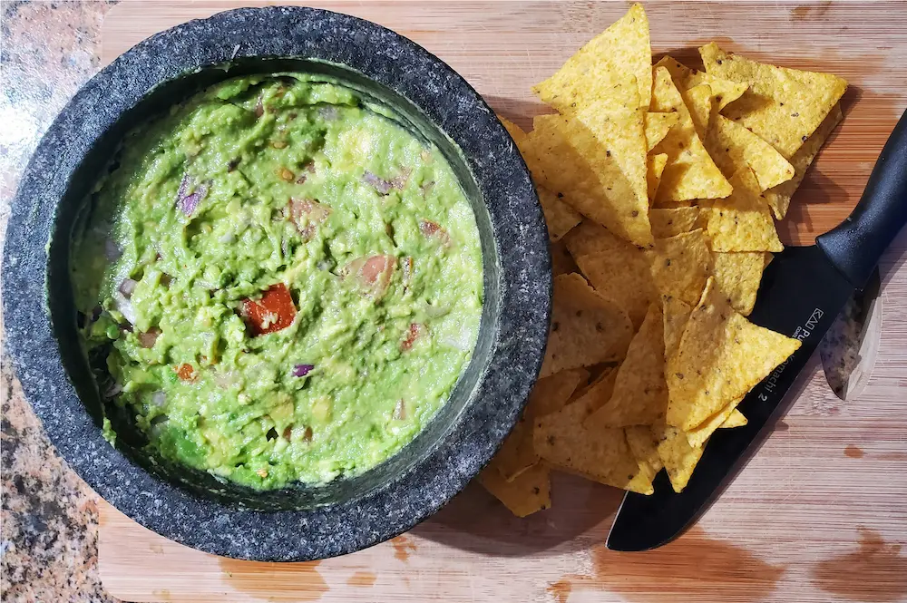 Guacamole fresco servido en un molcajete de piedra volcánica, preparado con aguacate machacado, jitomate, cebolla, cilantro, chile y limón, acompañado de totopos de maíz.