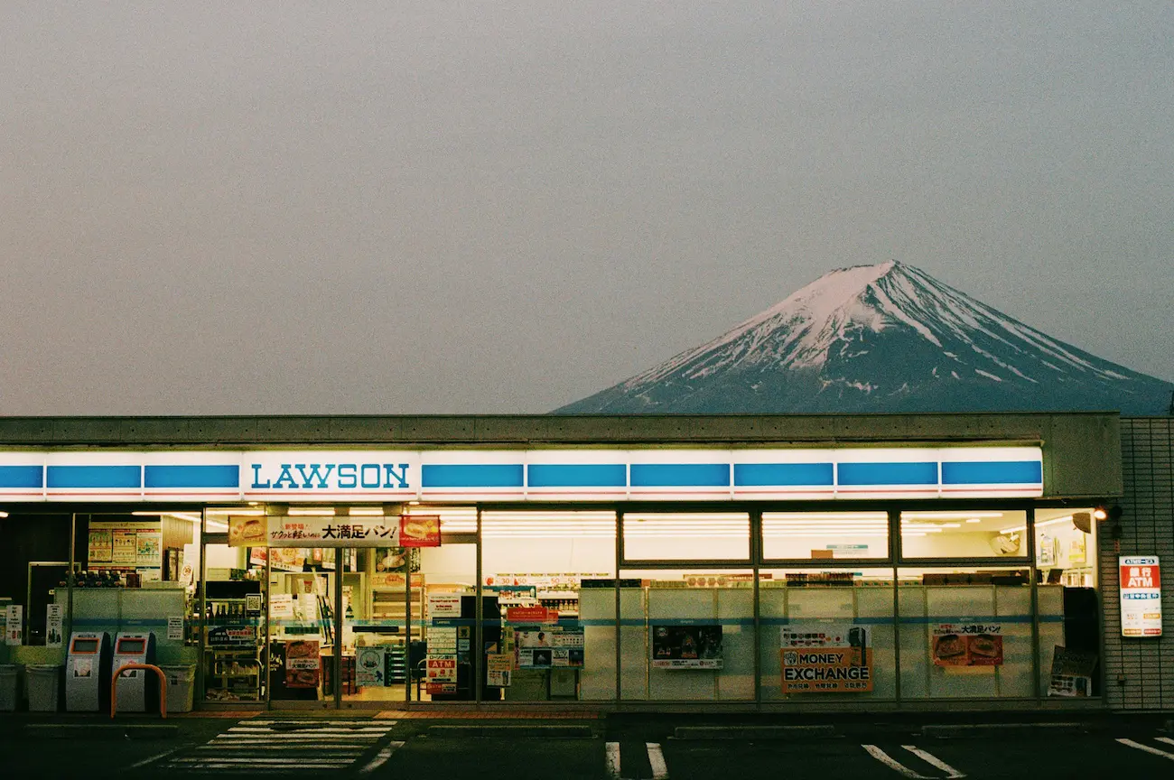 Fachada de una tienda Lawson en Kawaguchiko, Japón, con el Monte Fuji nevado apareciendo imponente justo detrás del edificio, en una de las fotos más virales del país
